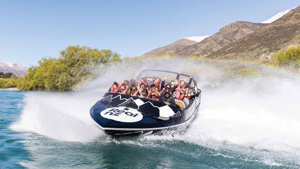 An excited crowd enjoy a 360 spin in the Queenstown Jet Boat, encompassed by a rainbow