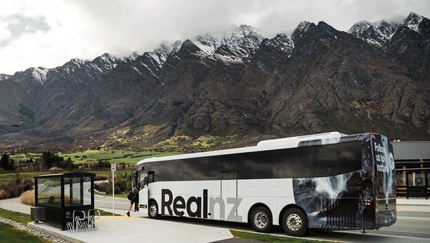 A RealNZ branded coach stops at the bottom of the snowy Remarkables mountain range