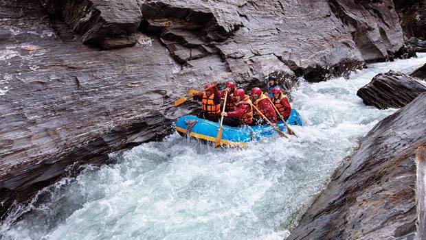 A group paddle furiously while rafting down a rapid on the Shotover River